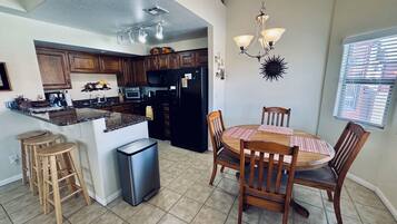 A kitchen with wooden cabinets, a central island, a dining table with chairs, a trash bin, and a chandelier.
