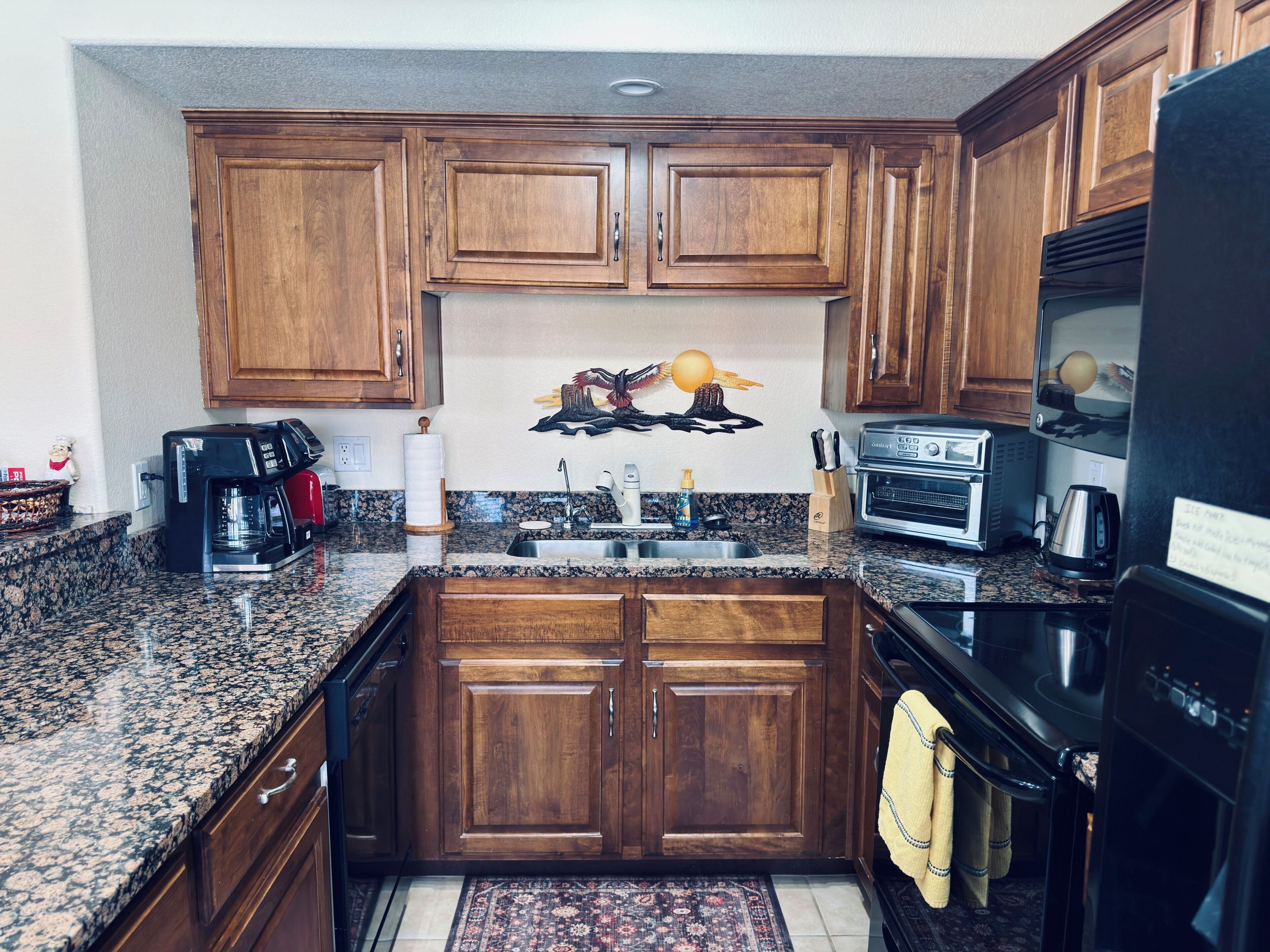 A kitchen with wooden cabinets, a granite countertop, a coffee maker, a toaster, and a refrigerator.