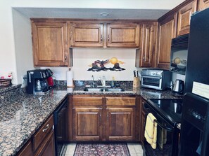A kitchen with wooden cabinets, a granite countertop, a coffee maker, a toaster, and a refrigerator. - Fox Run | 3BR Near Wolf Creek + Free Activities (Mesquite)