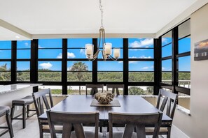 A dining area with a table and chairs, a chandelier, and large windows with a view of greenery.