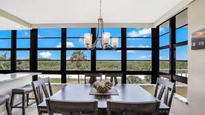 Zona pranzo con tavolo e sedie, un lampadario e ampie finestre che si affacciano sul verde.