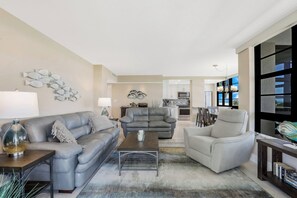 A modern living room with a grey sofa, a coffee table, and a dining area with chairs.
