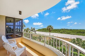 A balcony with white chairs, a view of the beach, and a clear sky.