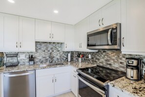 A modern kitchen with white cabinets, a stainless steel microwave, a built-in oven, and a granite countertop.