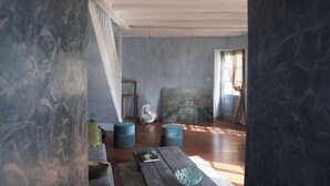 A room with wooden flooring, a large painting on the wall, and a fan in the corner. - La Maison d'à Côté (Taillebourg)