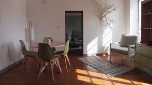 A dining area with a round table and chairs, a view of a room through a doorway, a branch decoration, and a window with natural light. - La Maison d'à Côté (Taillebourg)