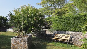 A stone bench in a garden with flowering plants and a stone wall. - La Maison d'à Côté (Taillebourg)