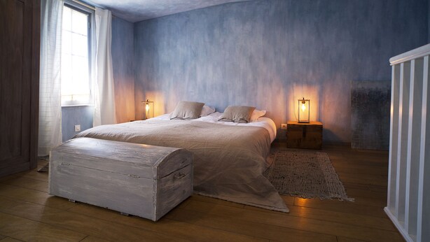 A bedroom with a large bed, wooden floor, and a nightstand with a lamp. - La Maison d'à Côté (Taillebourg)