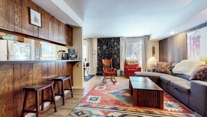 A cozy living room with a wooden bar area, a stone fireplace, a red armchair, and a grey sofa. - Central Location, Restaurants & Shops. Tennis Courts, Hot Tub & Pool On-site (Mammoth Lakes)