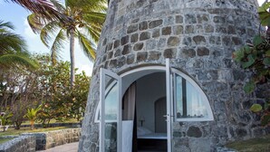 Un bâtiment en pierre doté d’une entrée circulaire, d’un lit à l’intérieur et offrant une vue sur des palmiers.