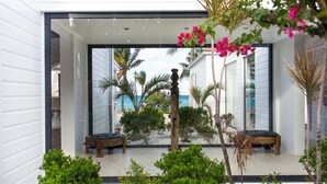Une maison moderne dotée d’une porte vitrée donnant sur un patio agrémenté de deux bancs en bois et d’un petit jardin.