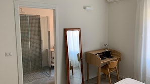 A hotel room with a shower, a desk with a chair, a bed, and a large mirror. - Flatty Alassio - Aloe (Alassio)