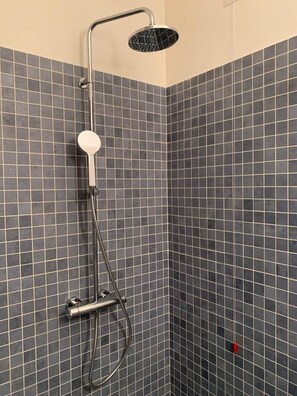Eine Dusche mit Duschbrause und Armatur an der Wand.