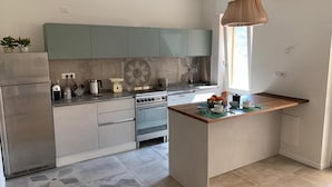 A modern kitchen with a central island, stainless steel appliances, and a window providing natural light. - Flatty Alassio - Aloe (Alassio)