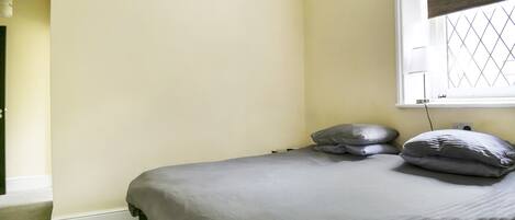 A bedroom with a bed, a window with a blind, and a door leading to another room.