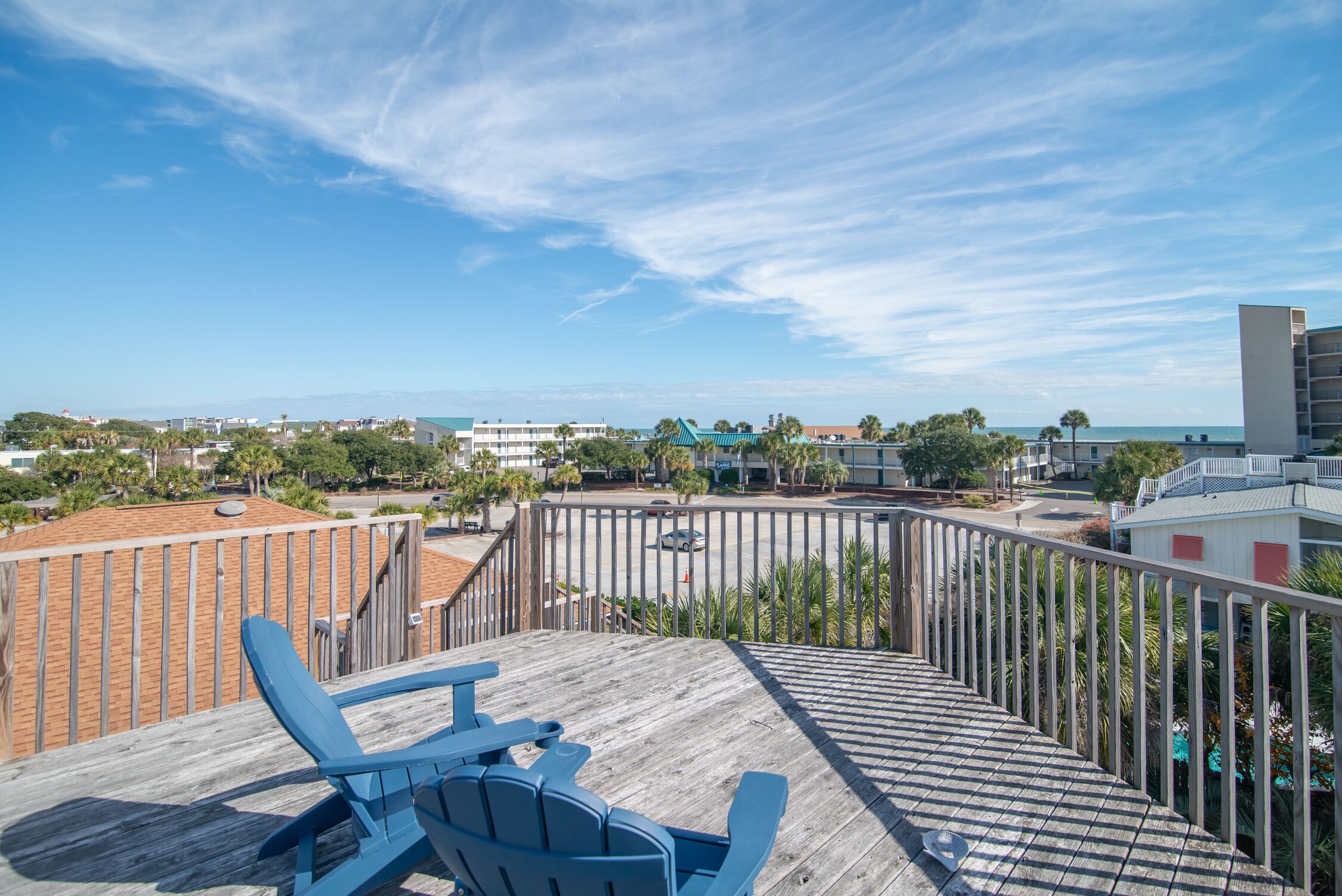 A wooden deck with a blue chair, overlooking a coastal area with buildings and a clear sky.