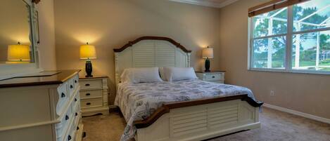 A bedroom with a bed, nightstands, a dresser, a ceiling fan, and a window with a view.