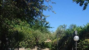 A paved pathway leading through a garden with a metal gate and a street lamp. - Sylviane House (Pietrabruna)
