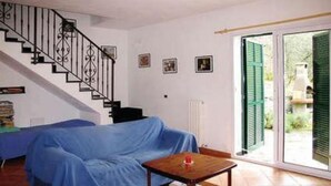 A room with a covered sofa, a small table, a staircase, and a view through a glass door. - Sylviane House (Pietrabruna)