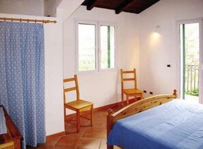 A bedroom with a bed, two wooden chairs, a window, and a curtain. - Sylviane House (Pietrabruna)