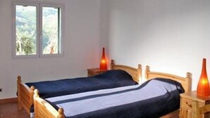 A double bed with a wooden headboard, a nightstand with a vase, and a window with a view of greenery. - Sylviane House (Pietrabruna)