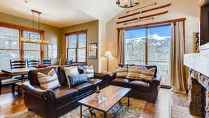 A spacious living room with leather sofas, a wooden coffee table, and large windows offering mountain views. - Walk to Lift | Heart of Main St | Pool | Hot Tubs! (Breckenridge)