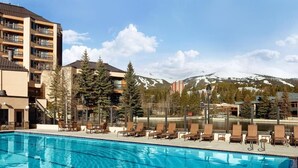 A swimming pool with lounge chairs, a mountain backdrop, and a multi-story building. - Walk to Lift | Heart of Main St | Pool | Hot Tubs! (Breckenridge)