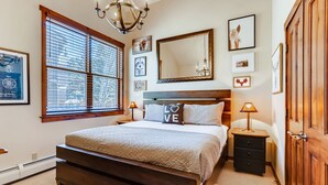 A bedroom with a bed, bedside tables, a dresser, a large window, and wall art. - Walk to Lift | Heart of Main St | Pool | Hot Tubs! (Breckenridge)