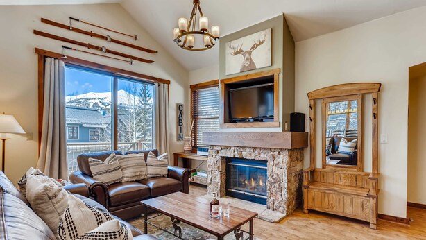 A living room with a stone fireplace, leather sofa, and a television mounted above it. - Walk to Lift | Heart of Main St | Pool | Hot Tubs! (Breckenridge)