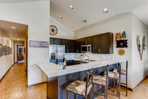 Une cuisine moderne avec des meubles de couleur sombre, un plan de travail blanc et un coin bar avec des tabourets.