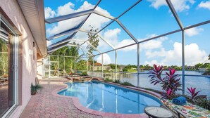A swimming pool with a glass enclosure, a patio area with a table and chairs, and a view of a lake. - Lakeside Living, Private Beach, Pool Table, Two Heated Pools - The Joint Venture - Roelens Vacations (Cape Coral)