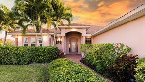 A house with a tiled roof, a central entrance, and a well-maintained garden with various plants and a lawn. - Lakeside Living, Private Beach, Pool Table, Two Heated Pools - The Joint Venture - Roelens Vacations (Cape Coral)
