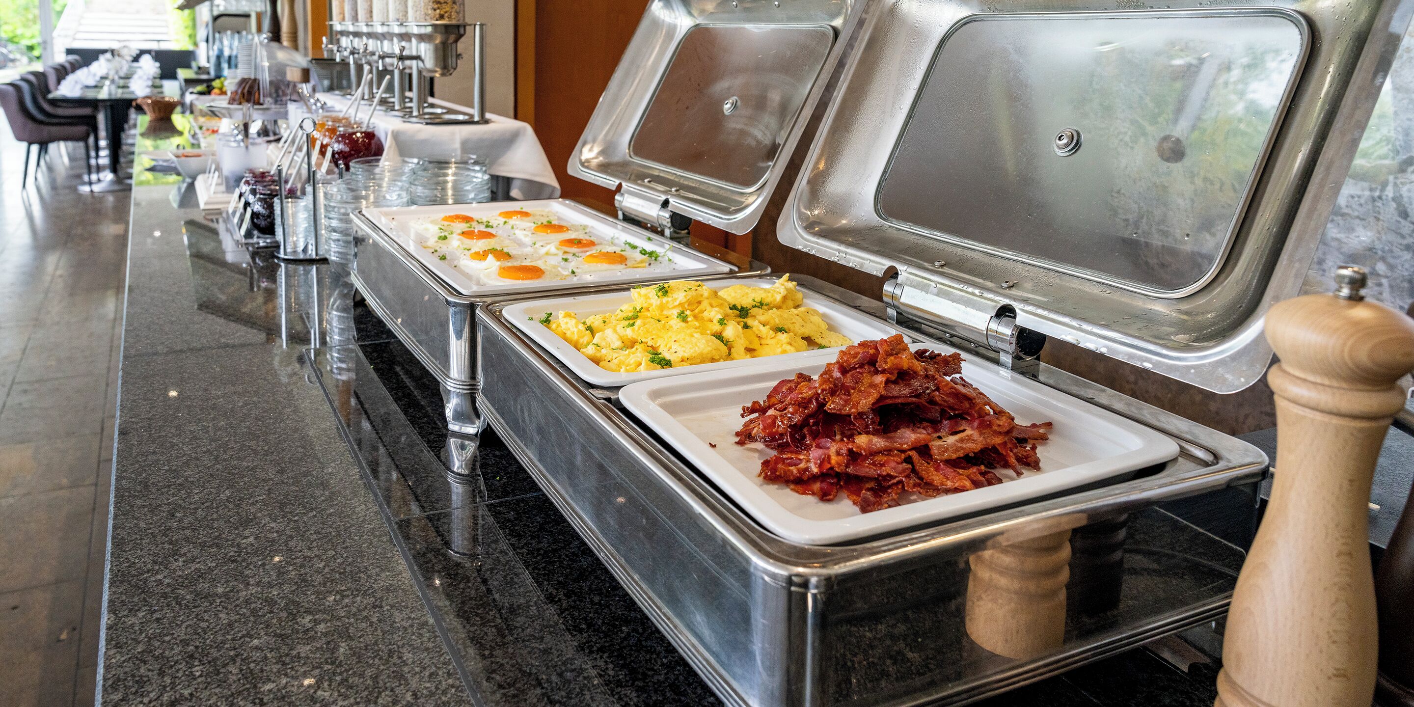 A buffet setup with various food items including scrambled eggs, hash browns, and bacon.