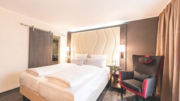 A hotel room with a large bed, a chair, a nightstand, and a mirror. - PLAZA Residence Stuttgart-Ditzingen (Ditzingen)