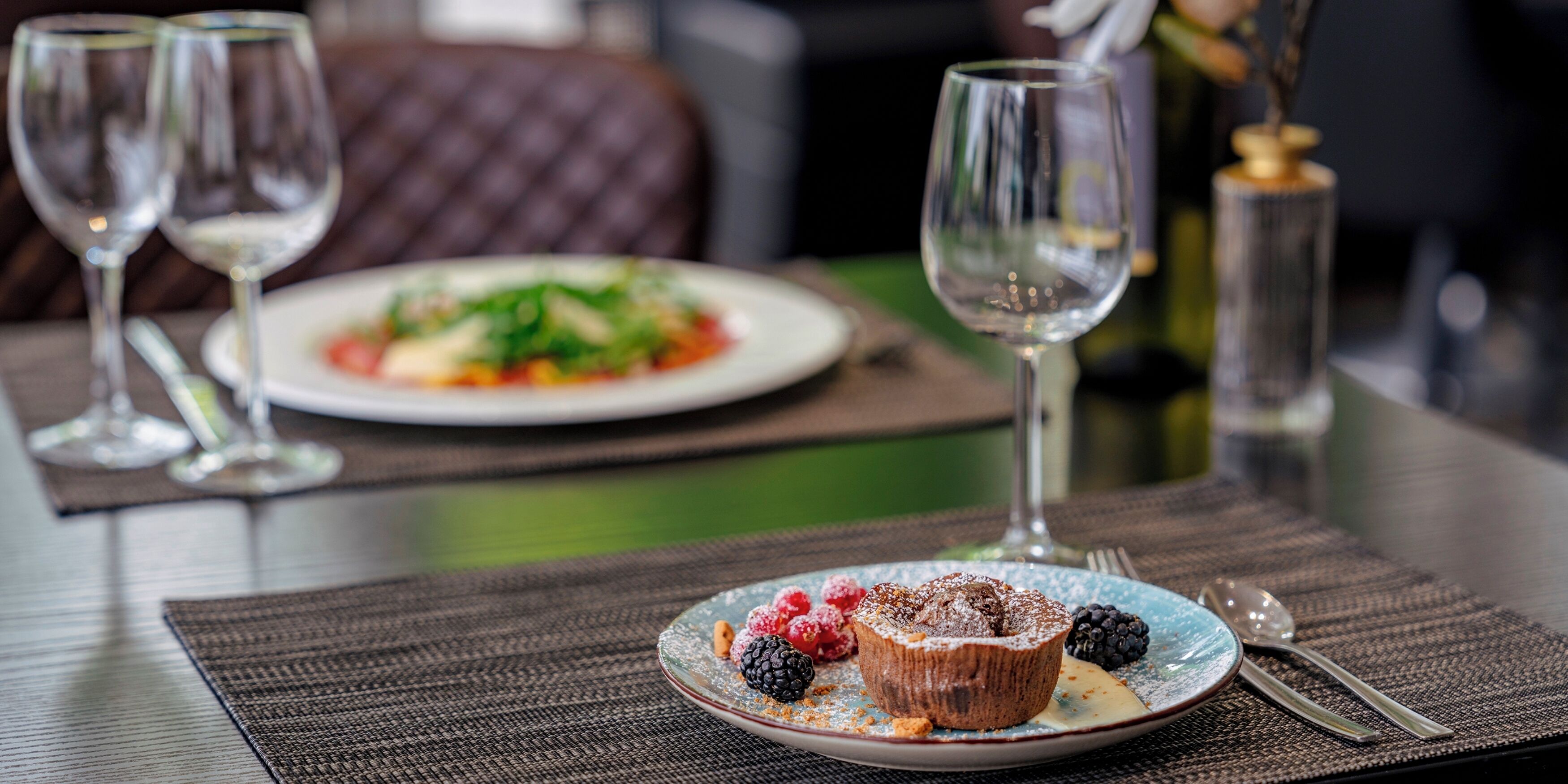 A dining table with a dessert plate, two wine glasses, and a bottle of wine.