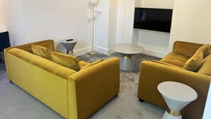 A living room with a yellow sofa set, a small round table, a floor lamp, and a flat-screen TV mounted on the wall. - The Mews, With Free Private Parking, Windermere (Windermere)