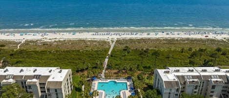 Een resort met een centraal gelegen zwembad, omringd door ligbedden en parasols, met uitzicht op een strand en de oceaan.