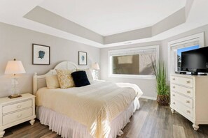 Un dormitorio con cama, mesitas de noche, cómoda, televisor y ventana.