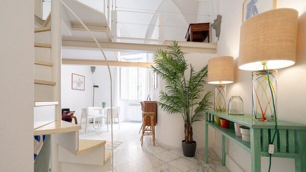 A modern interior with a staircase, a dining area, a potted plant, and a lamp on a console table.