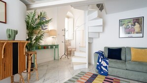 A living room with a sofa, a colorful striped rug, a green plant, a cactus, and a staircase.