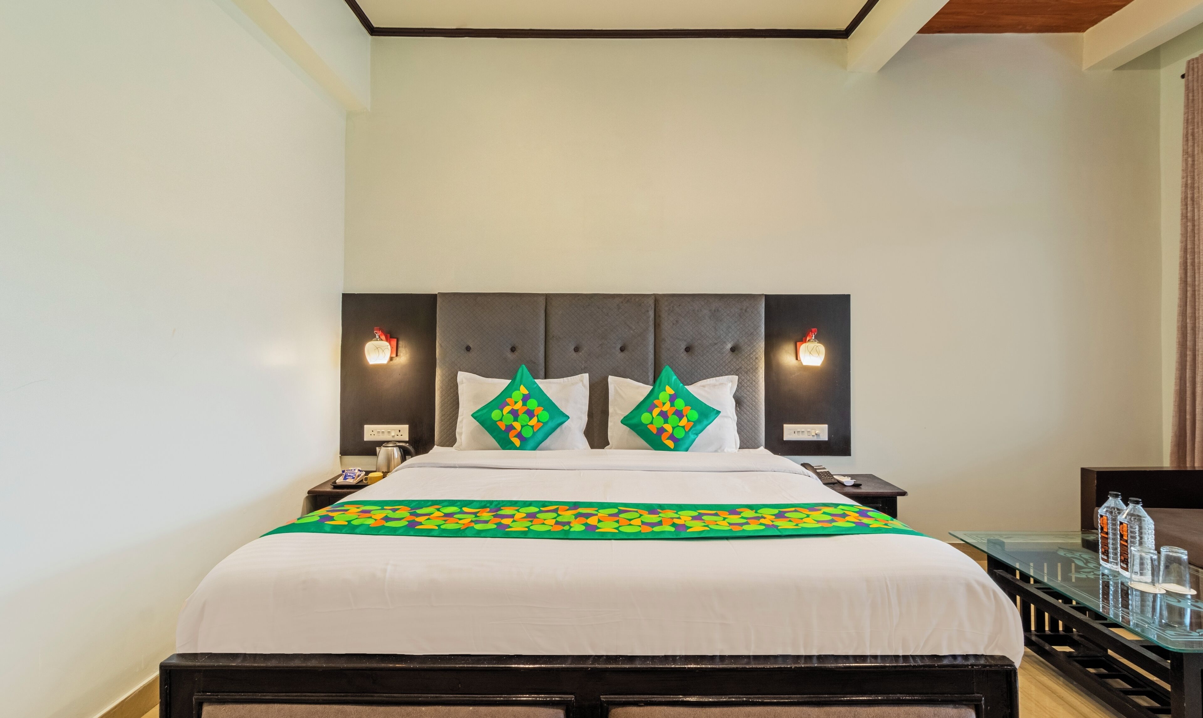 A hotel room with a large bed, two bedside tables, a nightstand, a glass coffee table, and a wall-mounted clock.