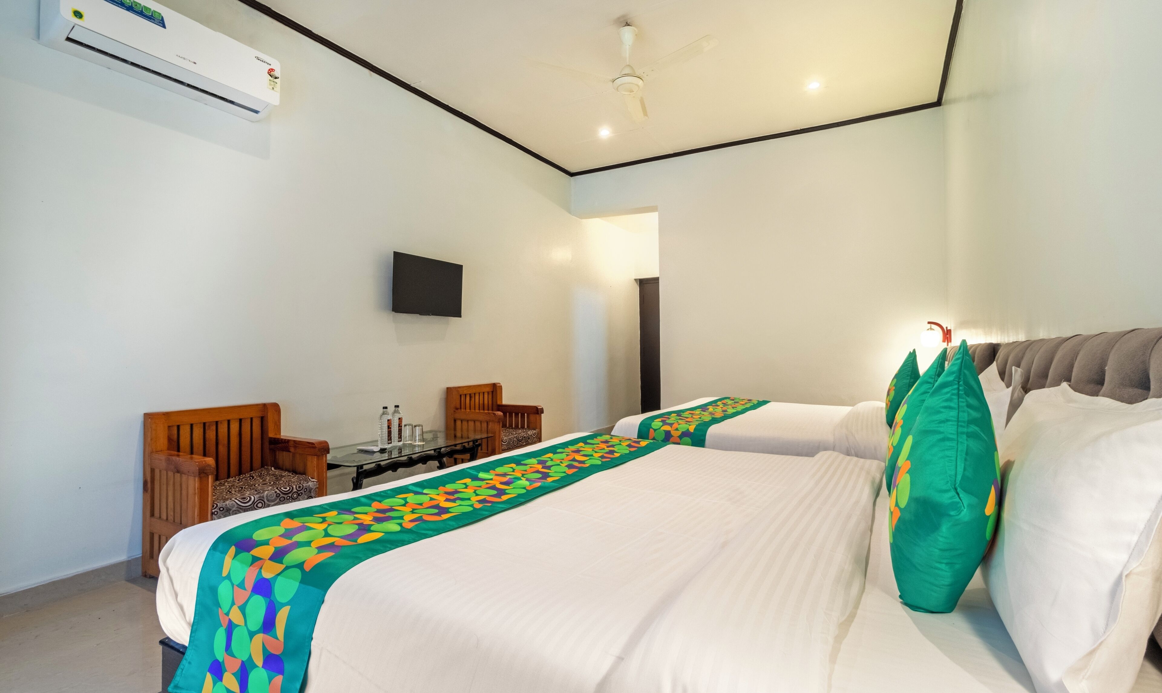 A hotel room with two beds, a flat-screen TV, a desk with chairs, and an air conditioning unit.