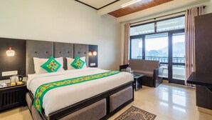 A hotel room with a large bed, a desk, a chair, and a view of the outdoors. - Treebo Spring Birds - 3Kms from Bhimtal Lake (Nainital)