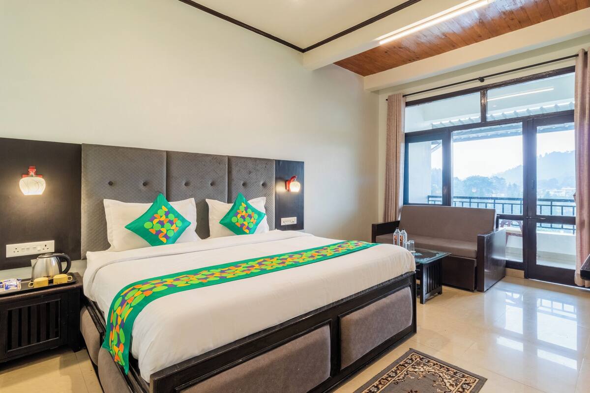 Quarto de hotel com cama grande, escrivaninha, cadeira e vista para o exterior.