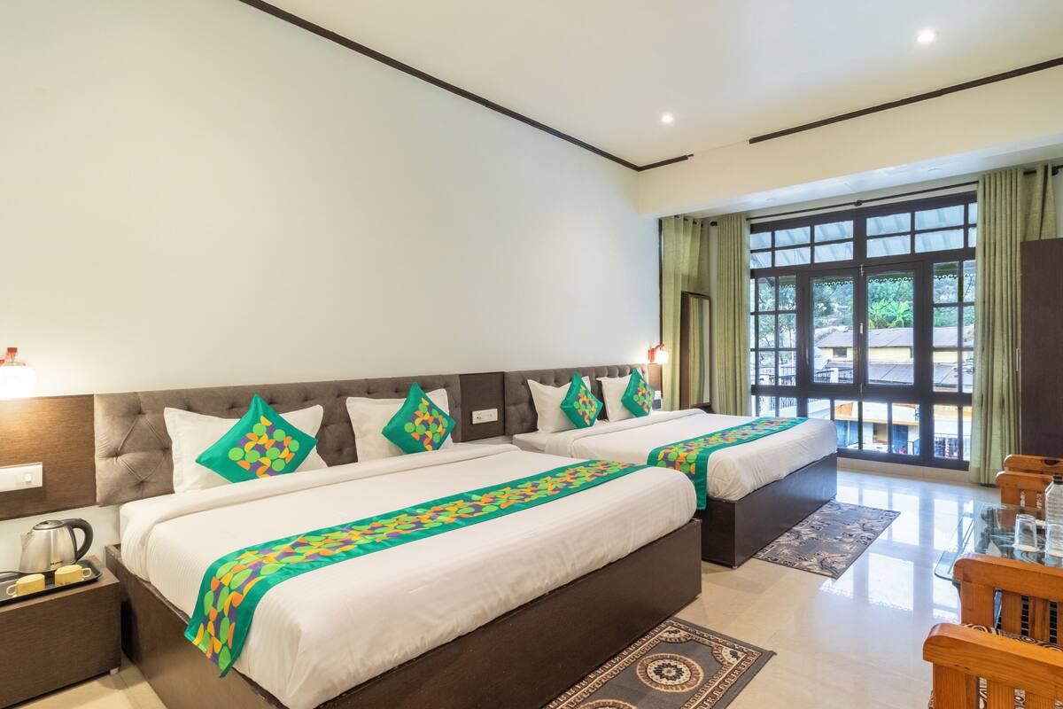 Quarto de hotel com duas camas, televisão, mesa de centro e vista para o exterior.