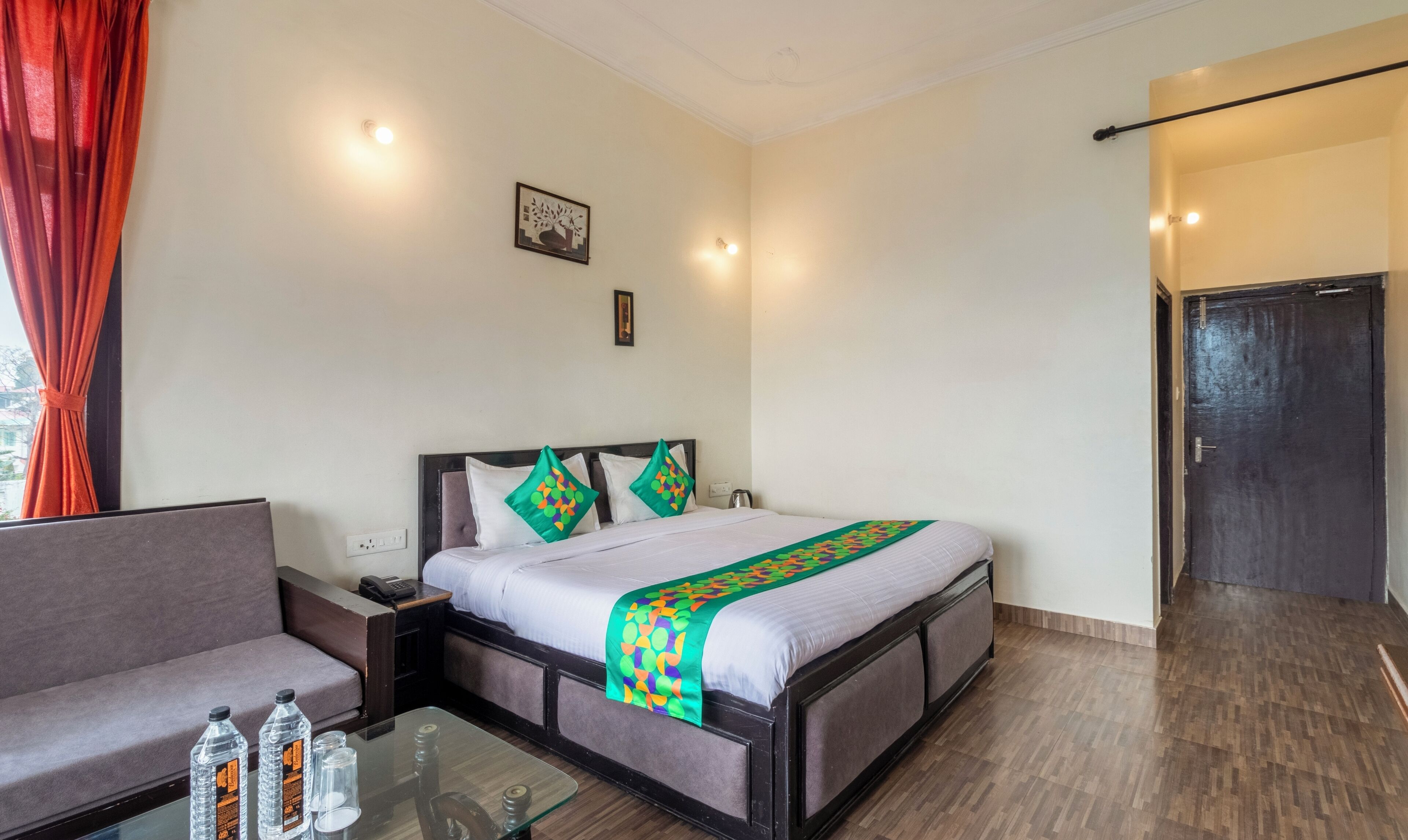 Ein Hotelzimmer mit Bett, Sofa, Glastisch und Wasserflaschen sowie einer Tür.