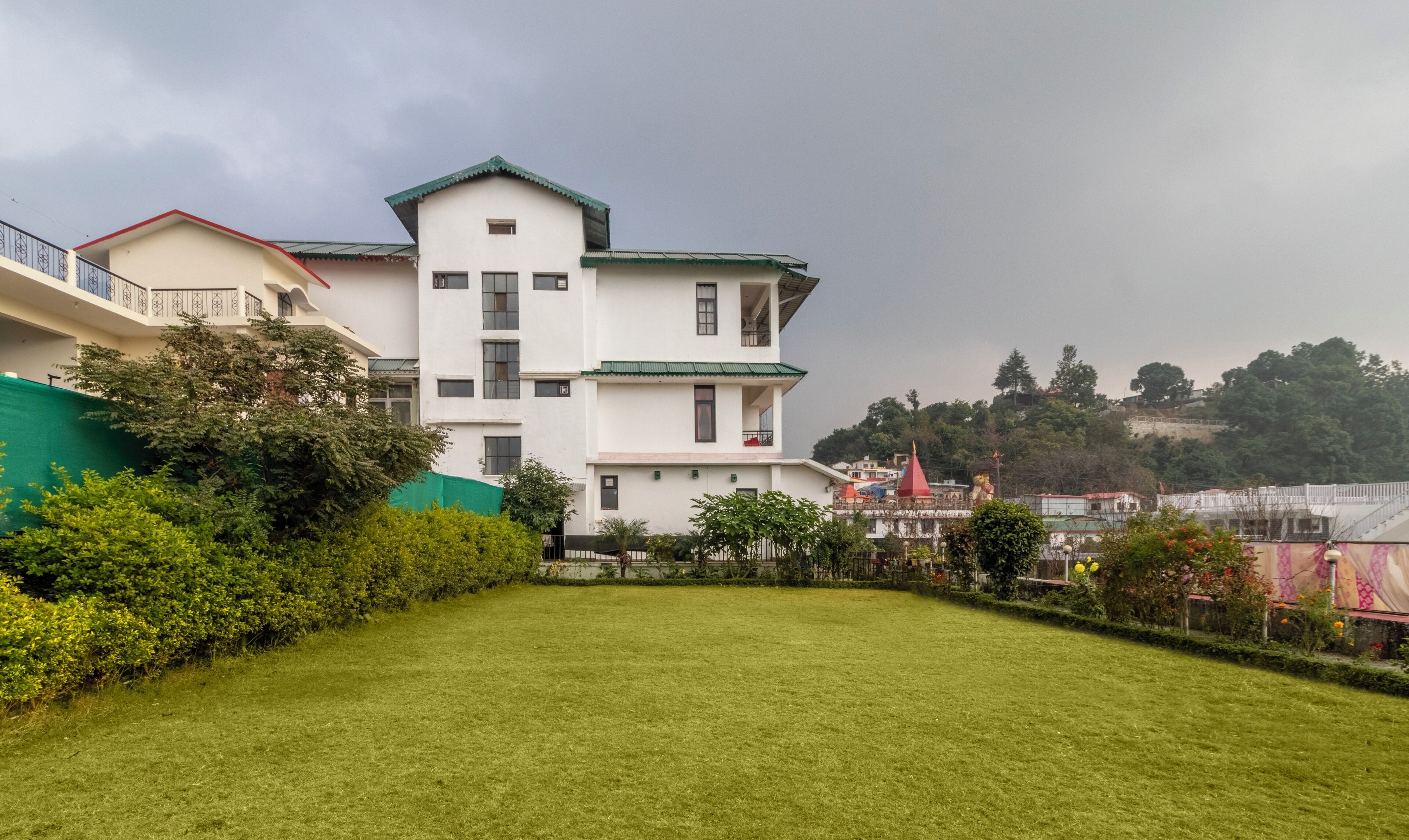 A multi-story building with a green roof, surrounded by well-maintained grass and bushes.