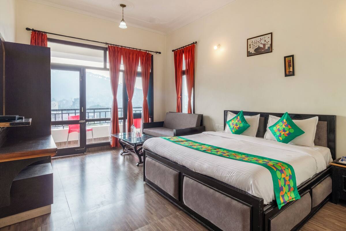 Quarto de hotel com uma cama, escrivaninha, cadeira e vista para o exterior.