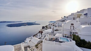 A white-washed building with a pool and outdoor seating, overlooking a calm sea and islands. - Santorini Mansion Maisonette Sea View Jacuzzi 3BDR (Thira - Santorini)