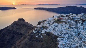 A coastal town with white buildings, a rocky cliff, and a calm sea at sunset. - Santorini Mansion Maisonette Sea View Jacuzzi 3BDR (Thira - Santorini)